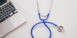 A laptop with a blue stethoscope on a white background, representing healthcare and technology.