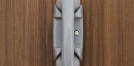 Close-up of a folded gray umbrella with a wooden handle, resting against a wooden door.