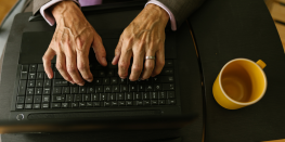 Overhead view of a person's hands typing on a laptop keyboard with a cup of coffee beside it.