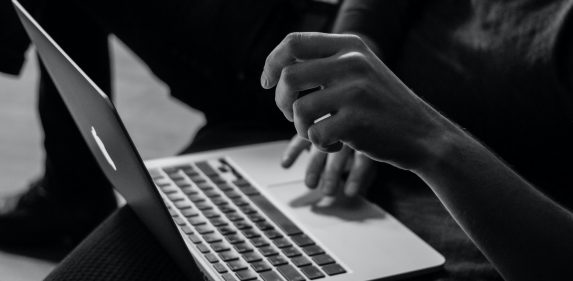 Black and white photo of a person's hands typing on a laptop keyboard.